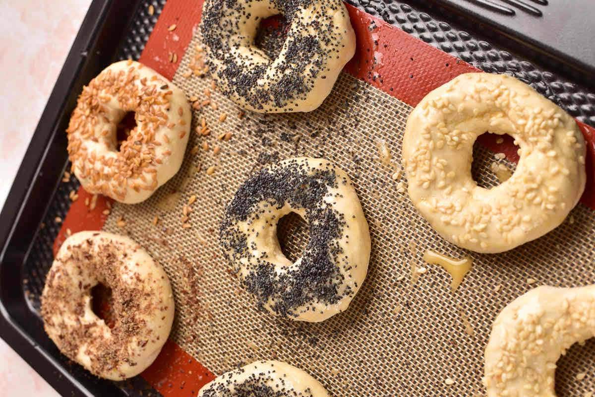 unbaked bagels with toppings on baking sheet.
