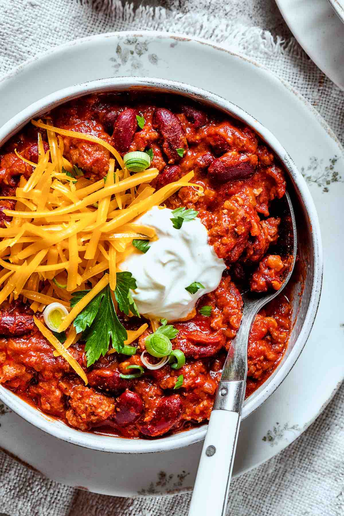 venison chili in a bowl with sour cream and shredded cheese.