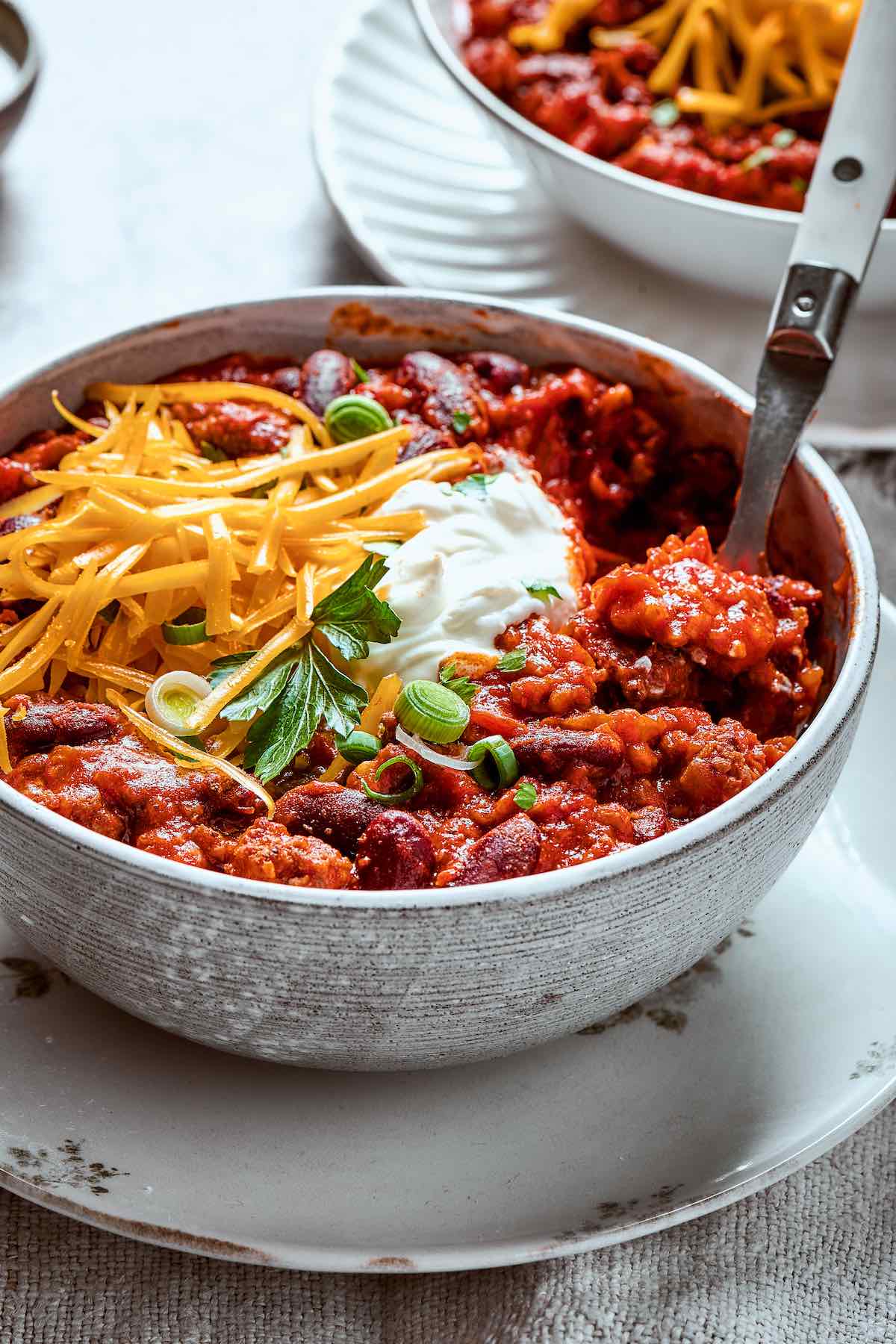 bowl of venison chili with sour cream and shredded cheese.
