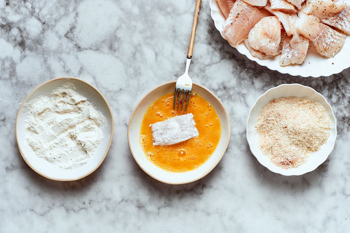 dipping seasoned fish in flour, egg wash, and bread crumbs.