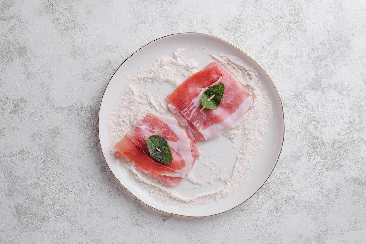 coating prepared saltimbocca in flour.