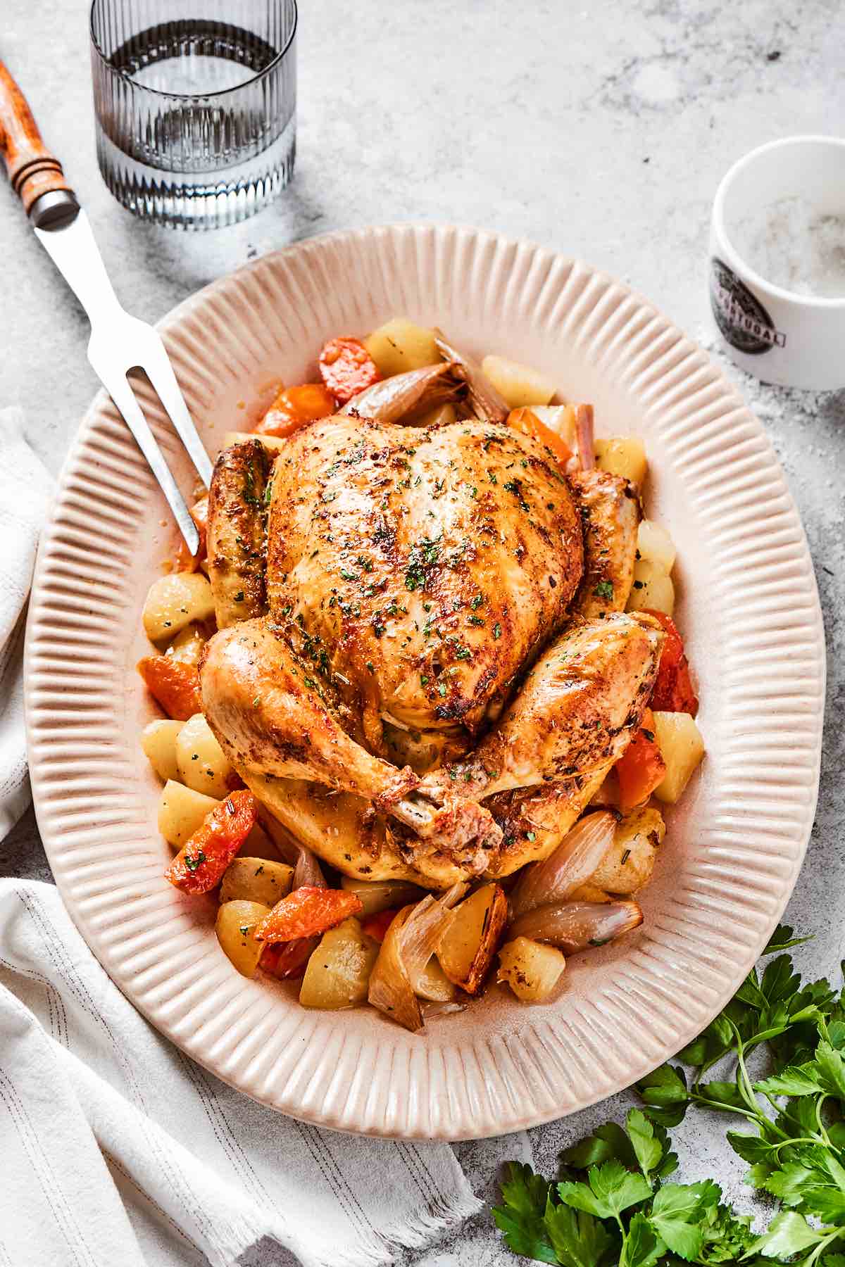 Dutch oven roasted chicken on a plate with root vegetables and potatoes.
