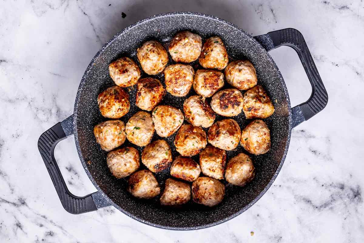 pork meatballs cooking in a skillet.