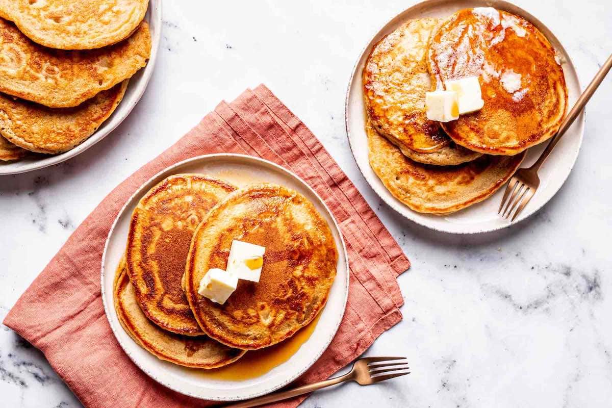 plates of oat milk pancakes with butter and maple syrup on top.