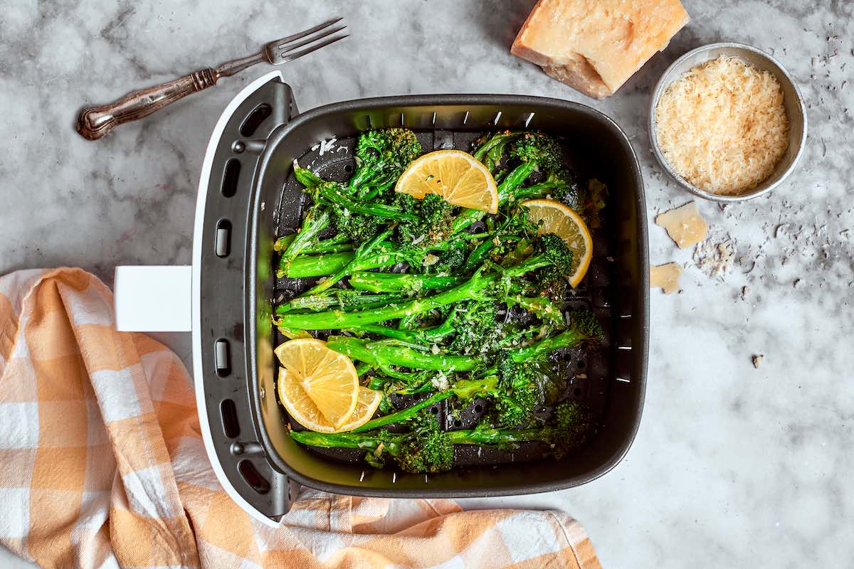 seasoned air fried broccolini with fresh lemon slices in the air fryer basket.