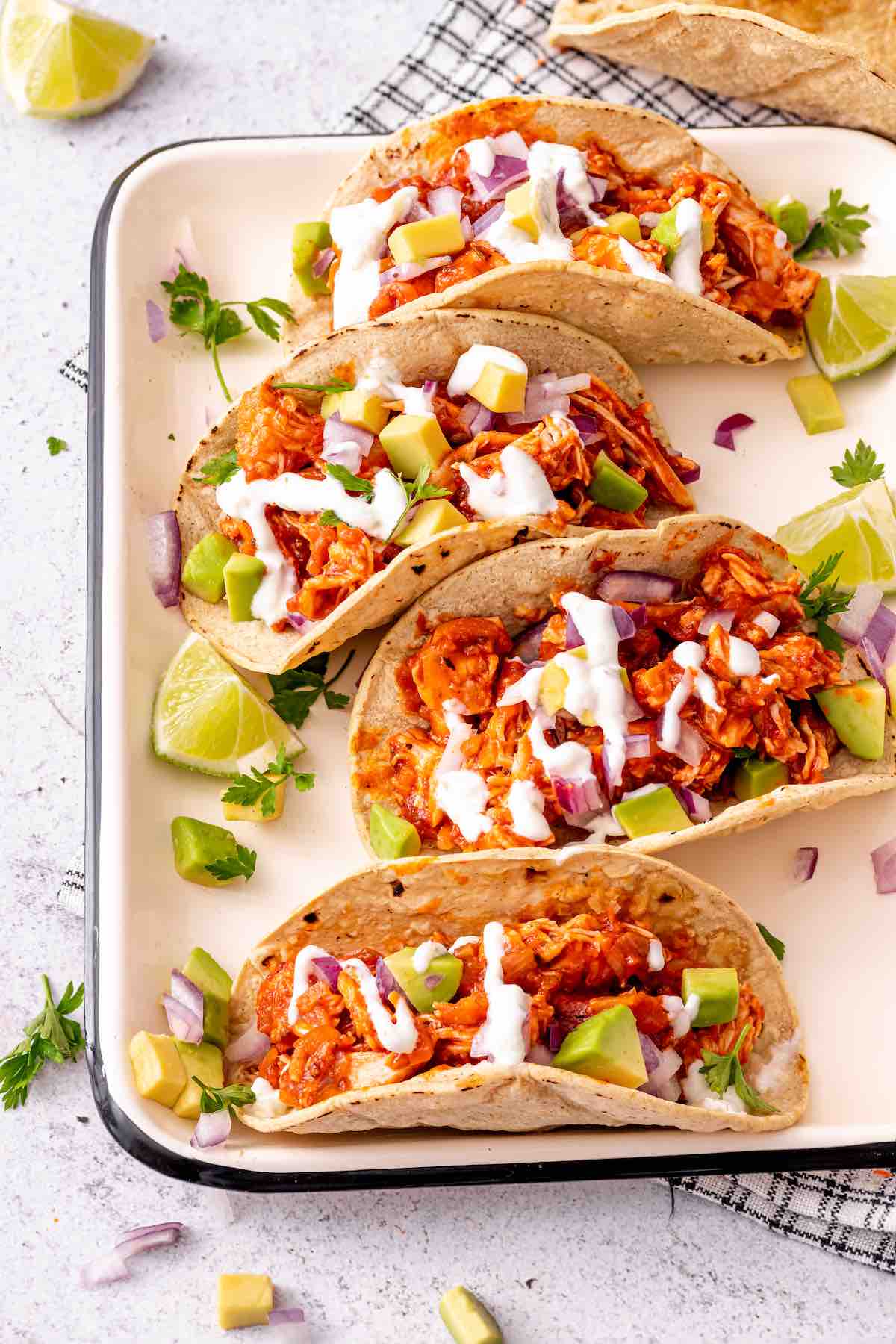 chicken tinga in soft tacos with avocado, cilantro, and crema.