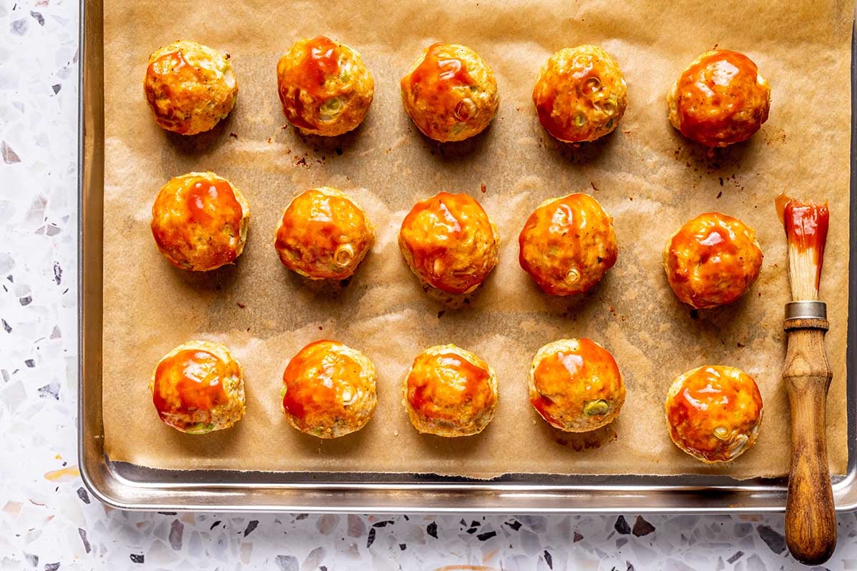 brushing meatballs with buffalo sauce.
