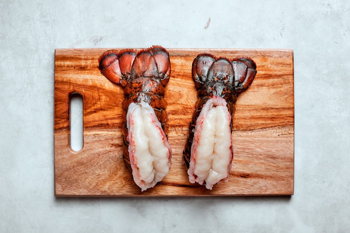 two lobster tails with their shells separated on a chopping board. 