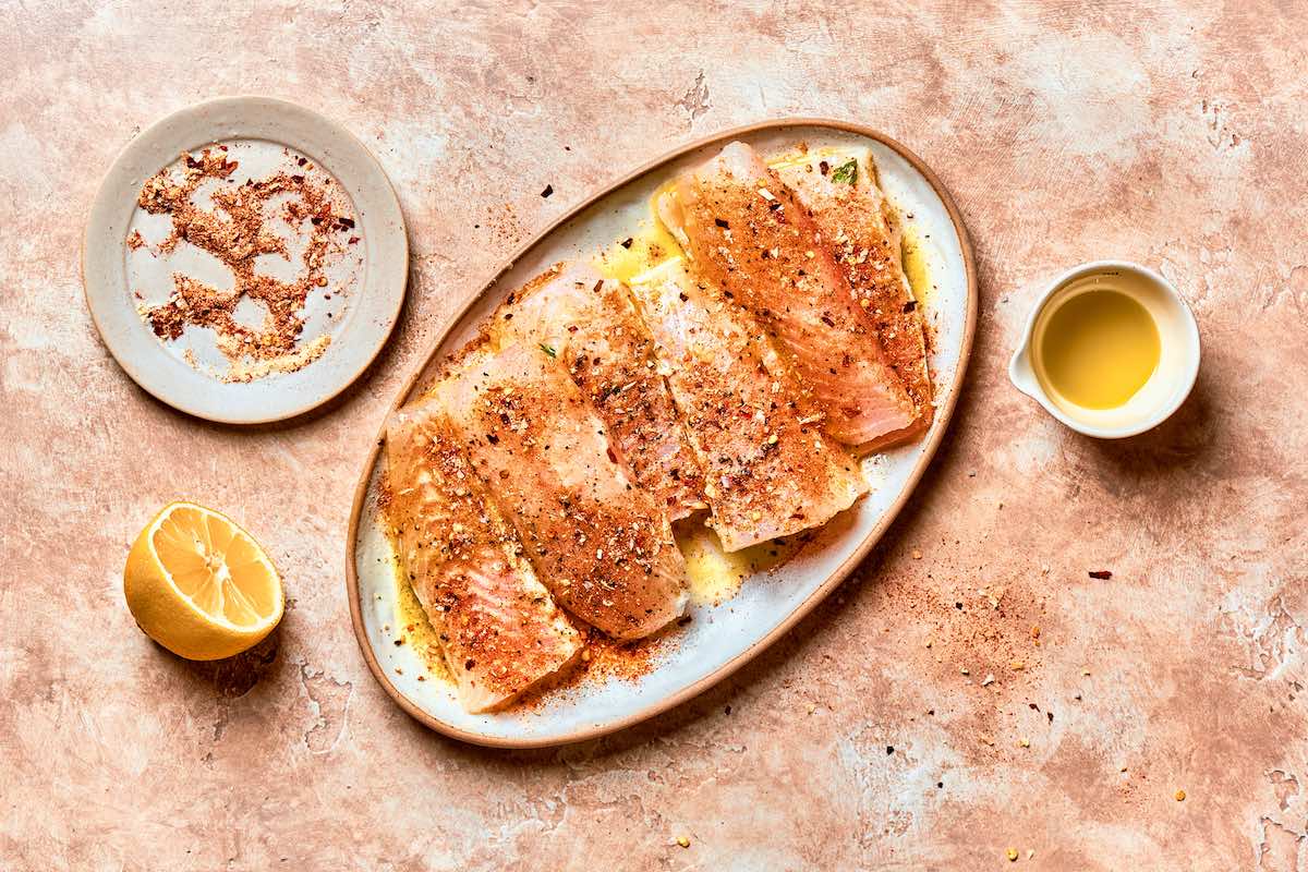 seasoned raw flounder fillets on a white plate.