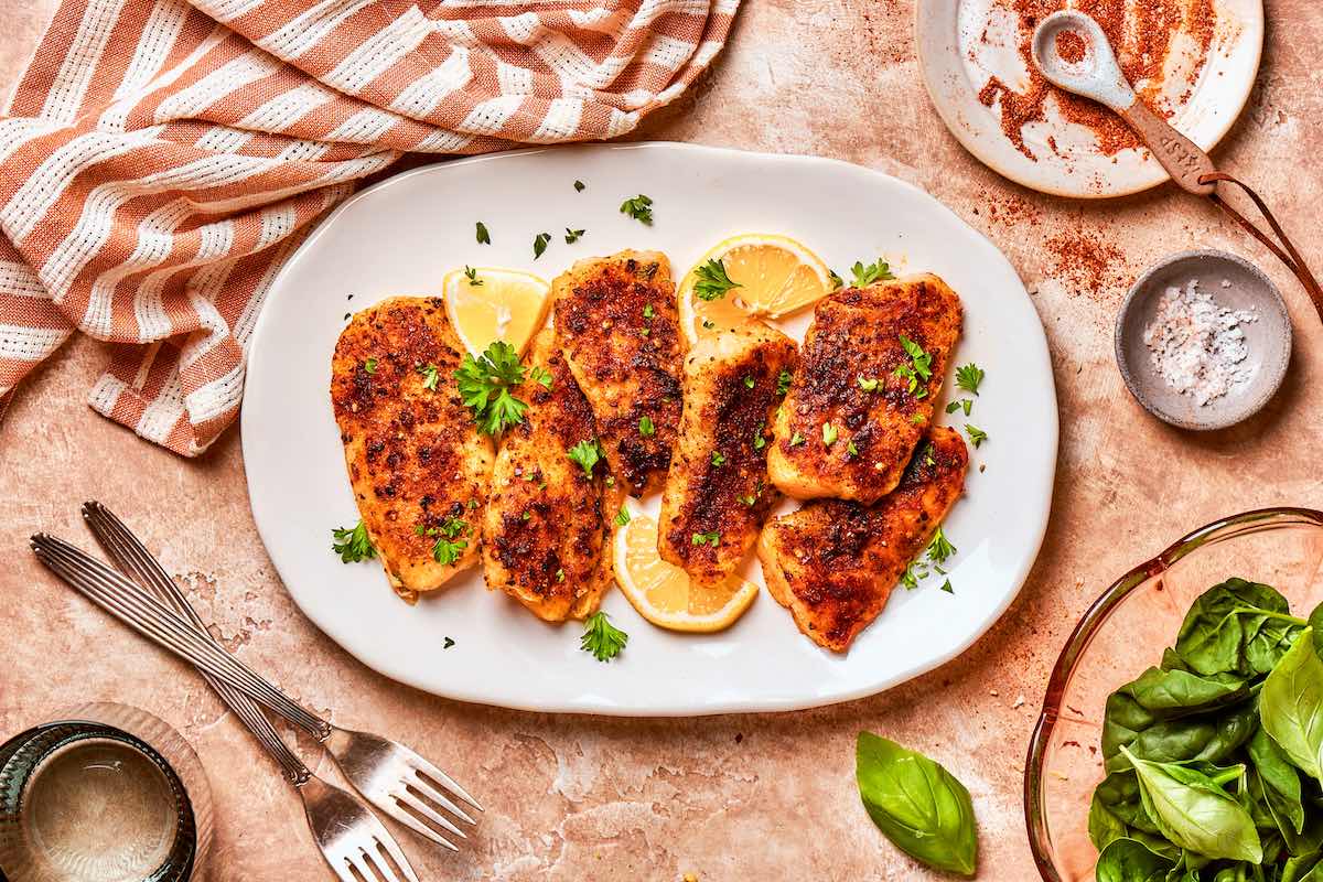air fried flounder on a white plate with fresh lemons and parsley.