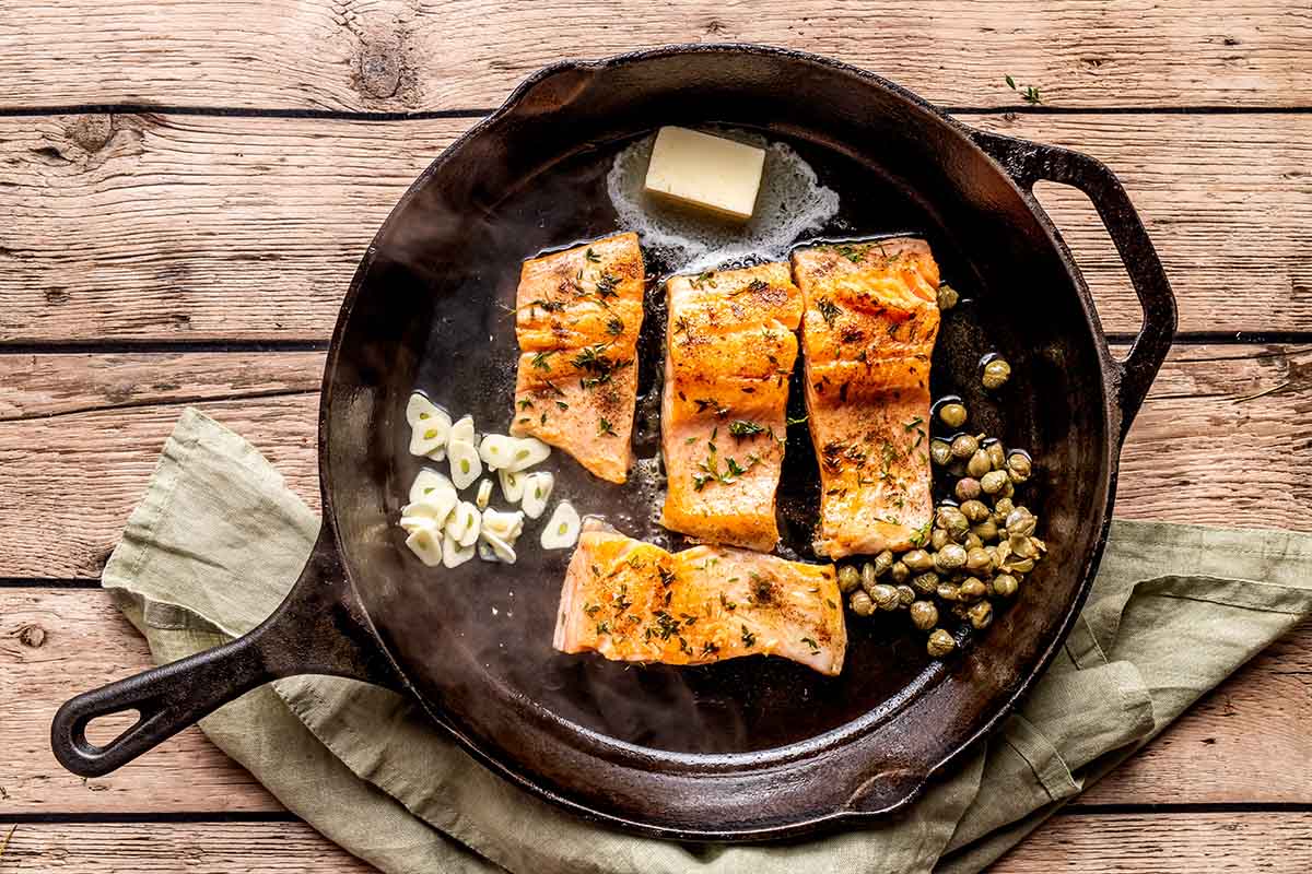 steelhead trout fillets in a skillet with garlic, butter, and capers.