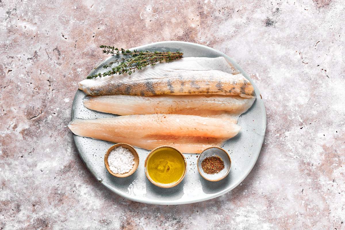 plate with raw perch fillets and small ramekins with salt, olive oil, and pepper.