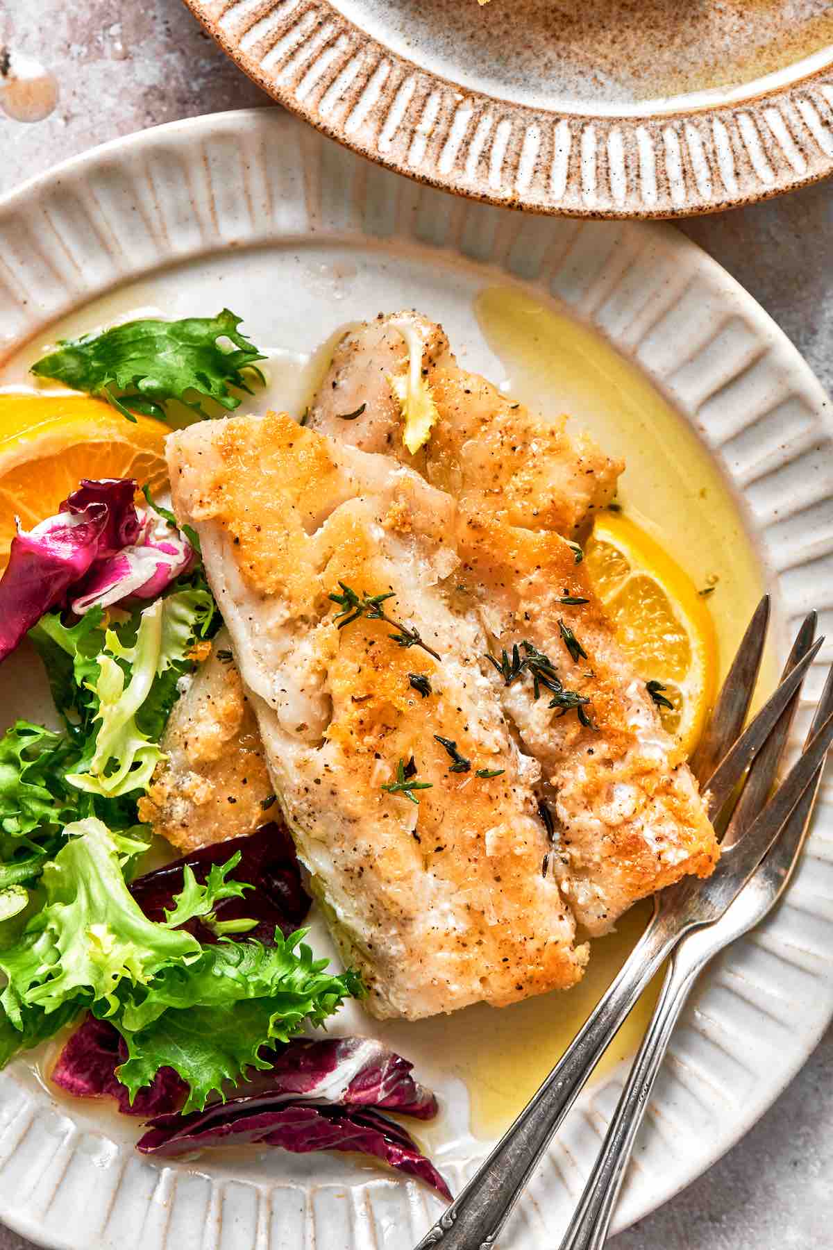 pan-fried perch over mixed green leaves on a white plate.