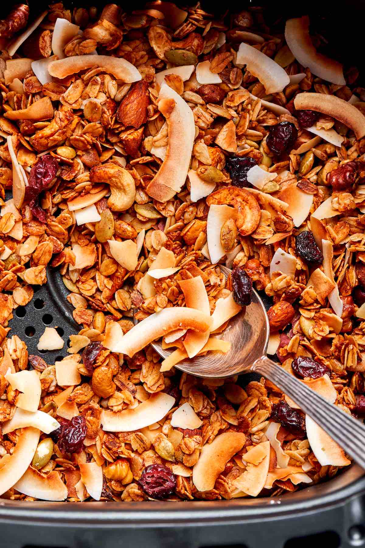 air fryer granola in the air fryer basket with a spoon showing texture.