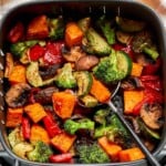 Close up of air fryer vegetables showing caramelized broccoli, sweet potato, mushrooms, zucchini, and red bell pepper topped with freshly grated Parmesan cheese.