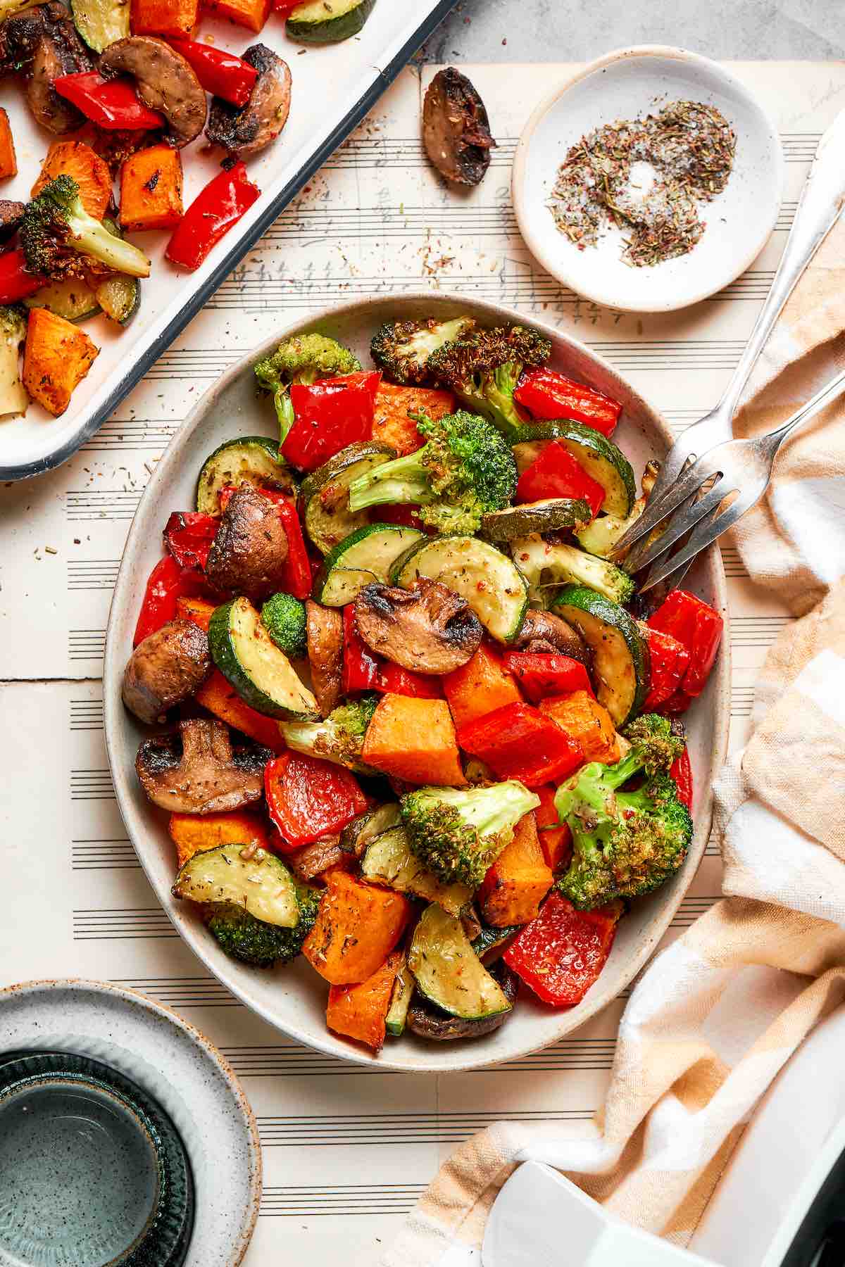Air fryer vegetables with broccoli, sweet potato, zucchini, mushrooms, and red bell pepper in a white oval bowl with serving forks.