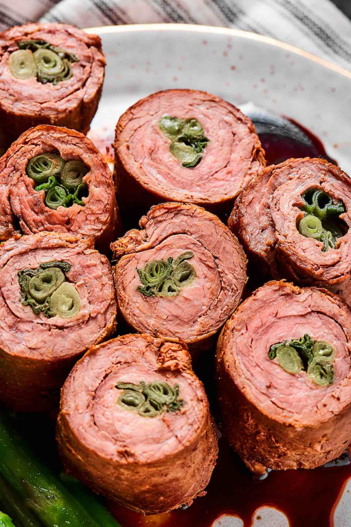 Beef negimaki rolls stacked showing medium rare beef and scallion centers in teriyaki sauce.