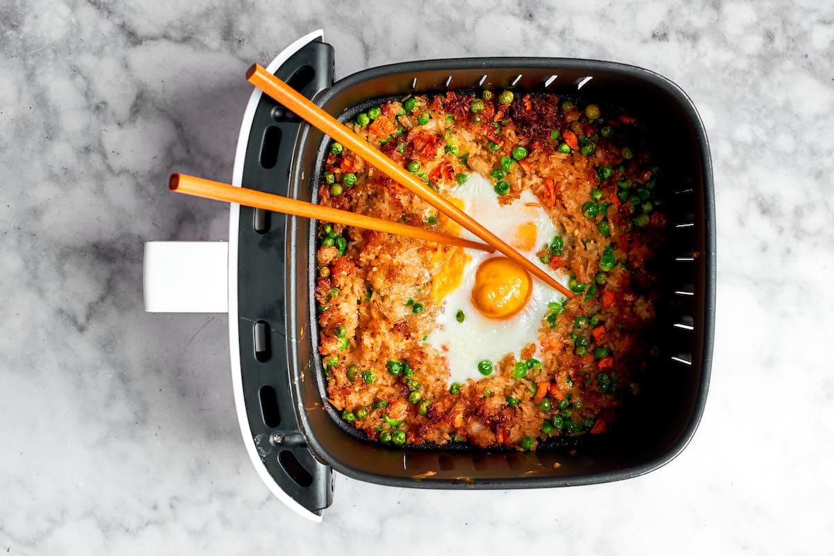 Mixing cooked egg into rice in air fryer.