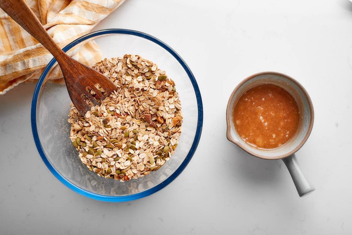 oats, nuts, and seeds in one bowl with maple syrup, coconut oil, and honey in another bowl.