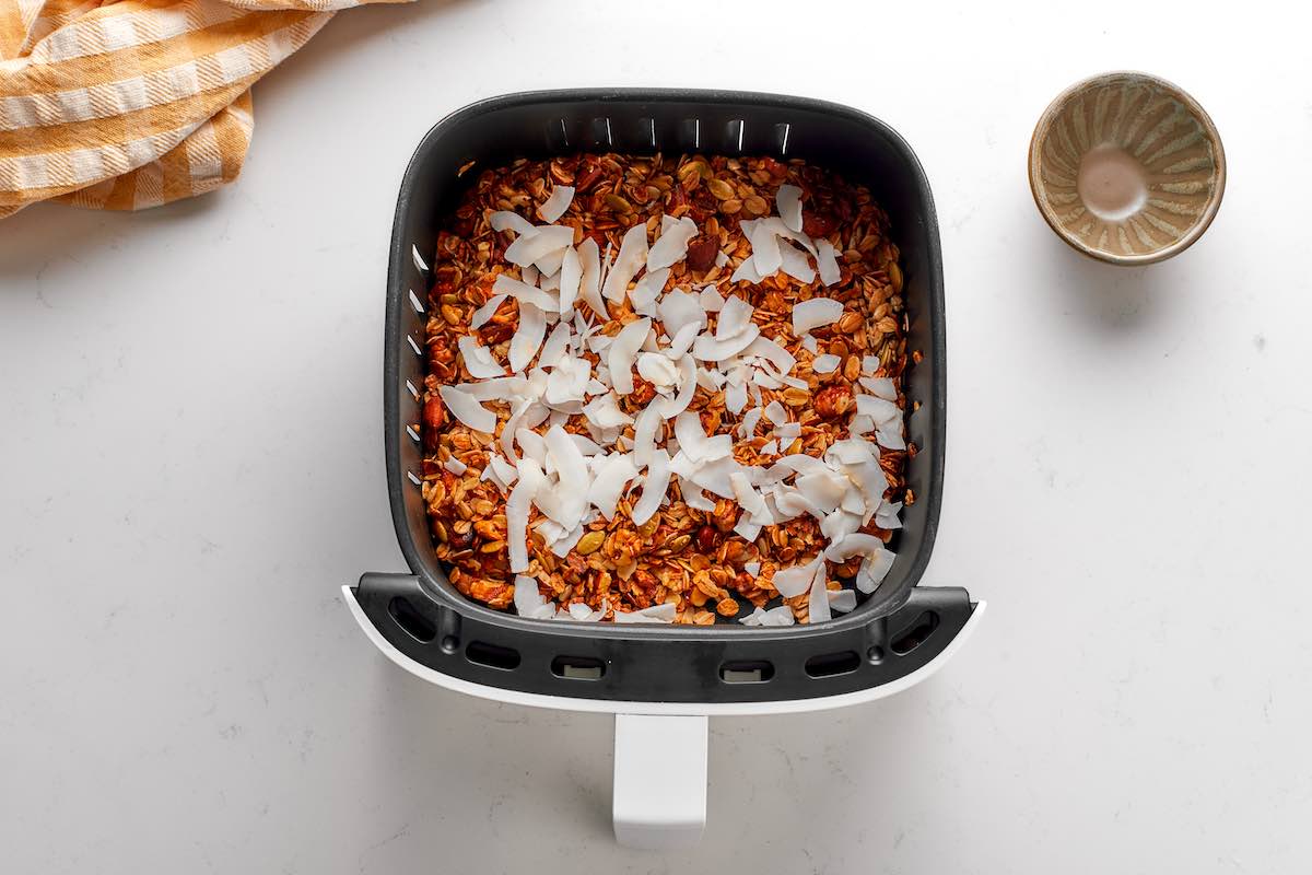 granola in the air fryer with a layer of shredded coconut on top.