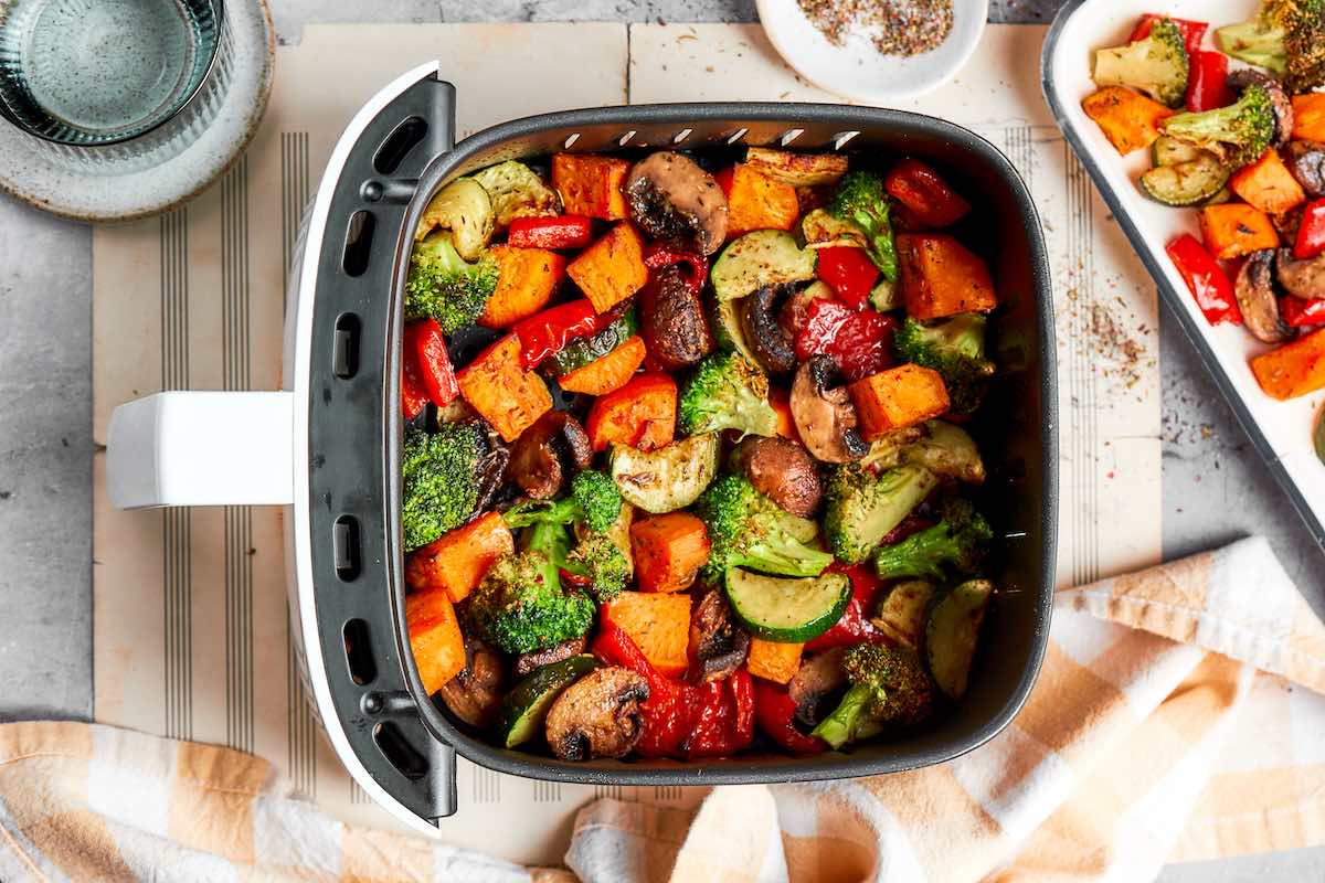 Cooked air fryer vegetables with caramelized edges in a white and black air fryer basket.