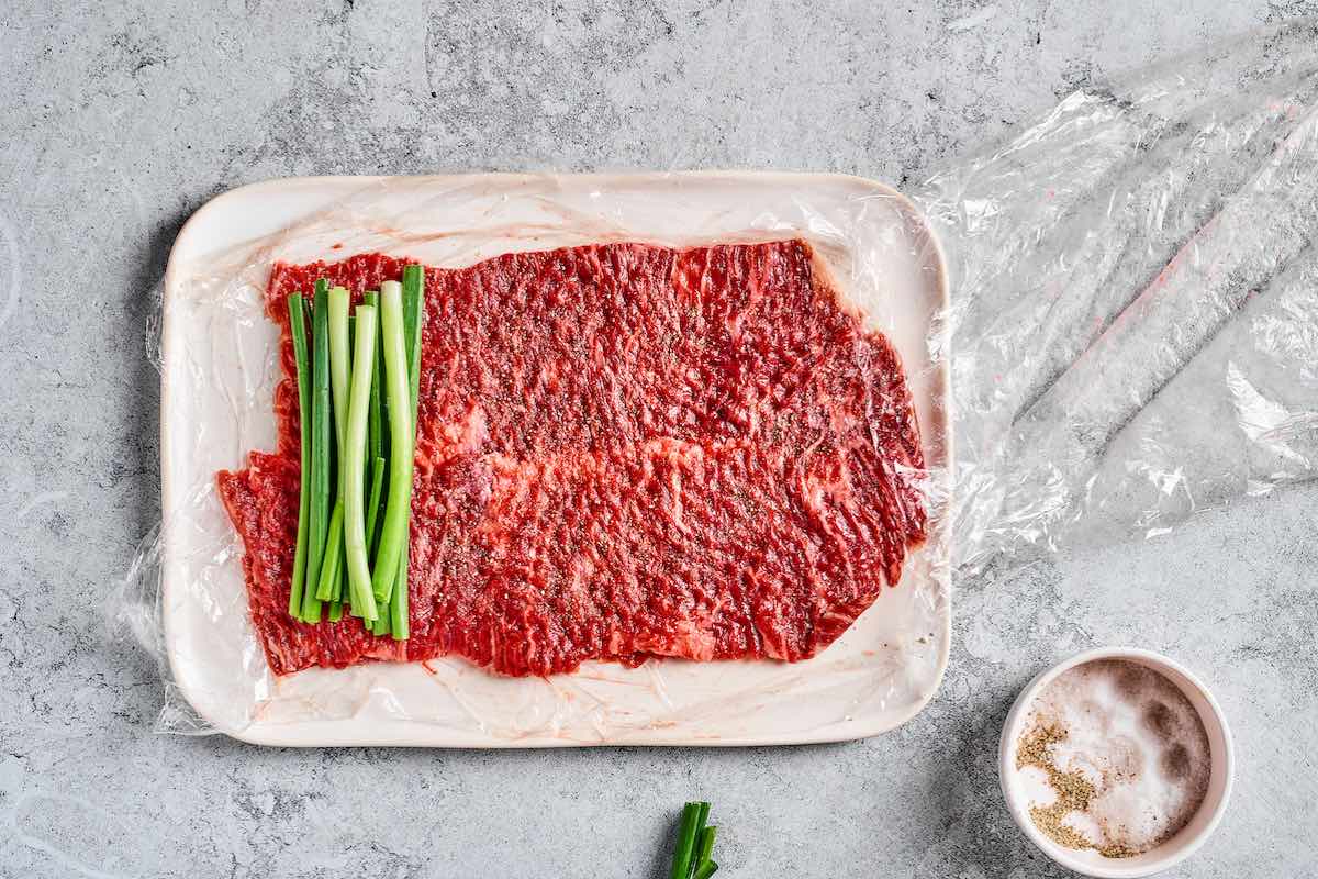 Thinly pounded flank steak with scallions placed at one edge ready to be rolled into beef negimaki.