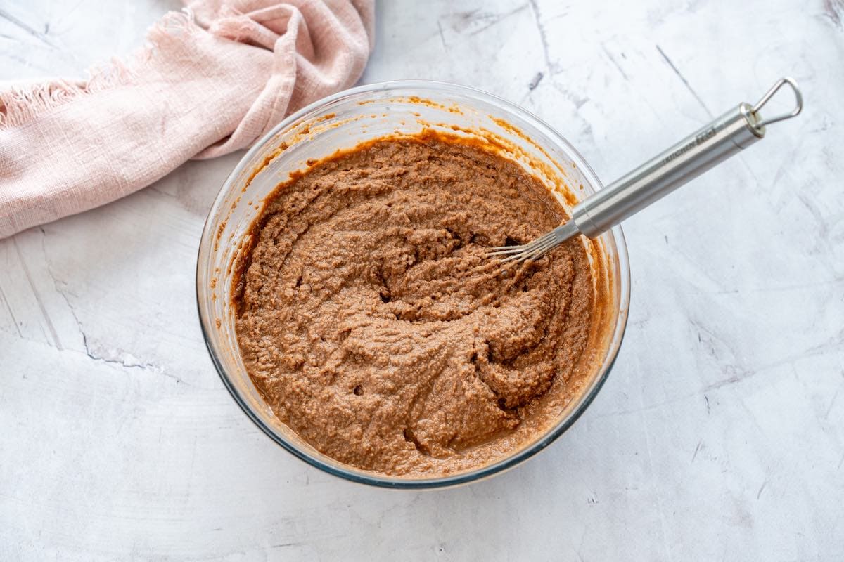 chocolate coconut flour cake batter in a clear mixing bowl with a whisk in the center.