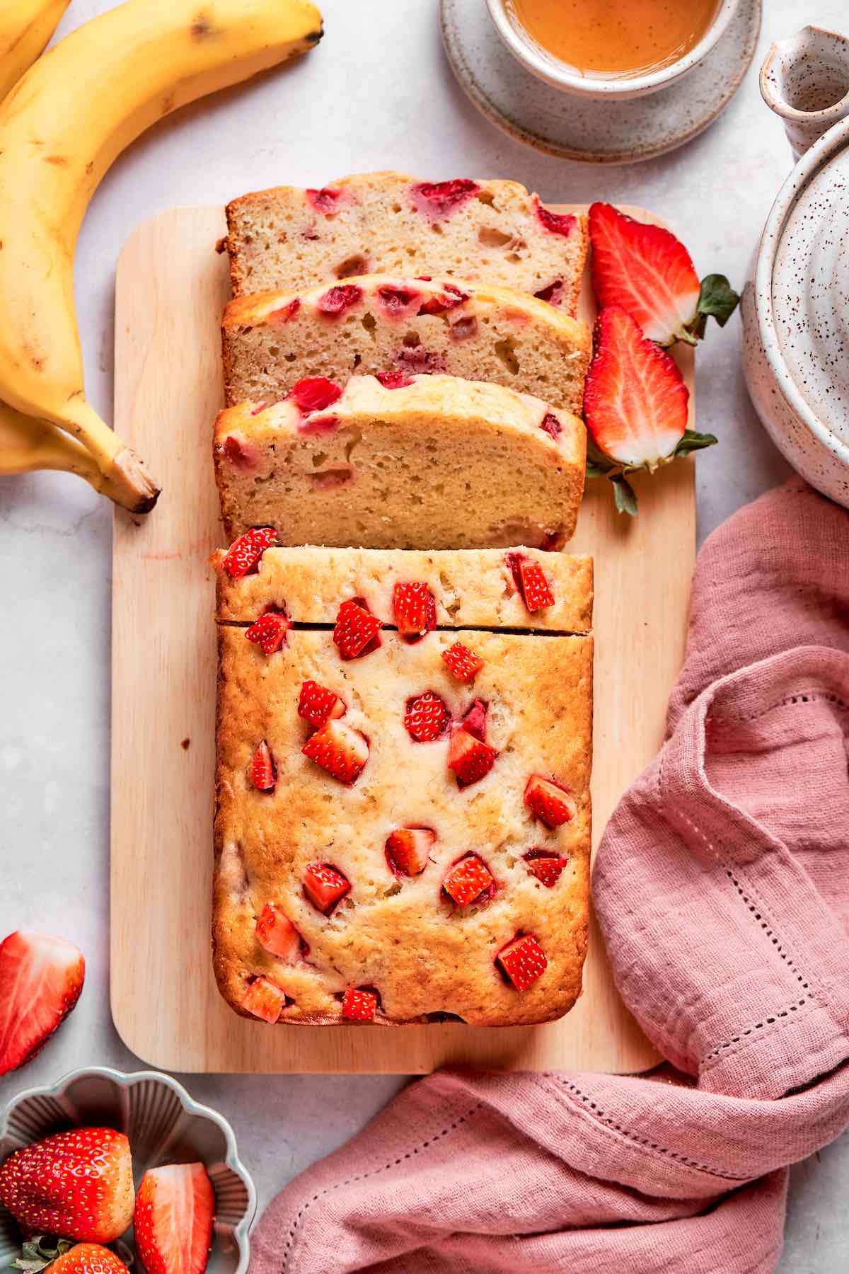 sliced strawberry banana bread on a wooden board.