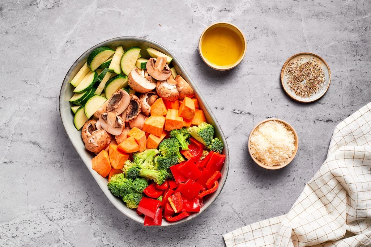 Air fryer vegetables ingredients including zucchini, mushrooms, sweet potato, broccoli, and red bell pepper with olive oil, seasoning, and Parmesan cheese.
