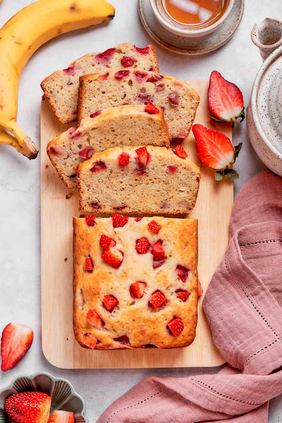 strawberry banana bread sliced on a wooden board with fresh strawberries decorated around it.