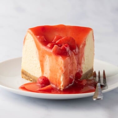 air fryer cheesecake recipe on a white plate with strawberry sauce on top.