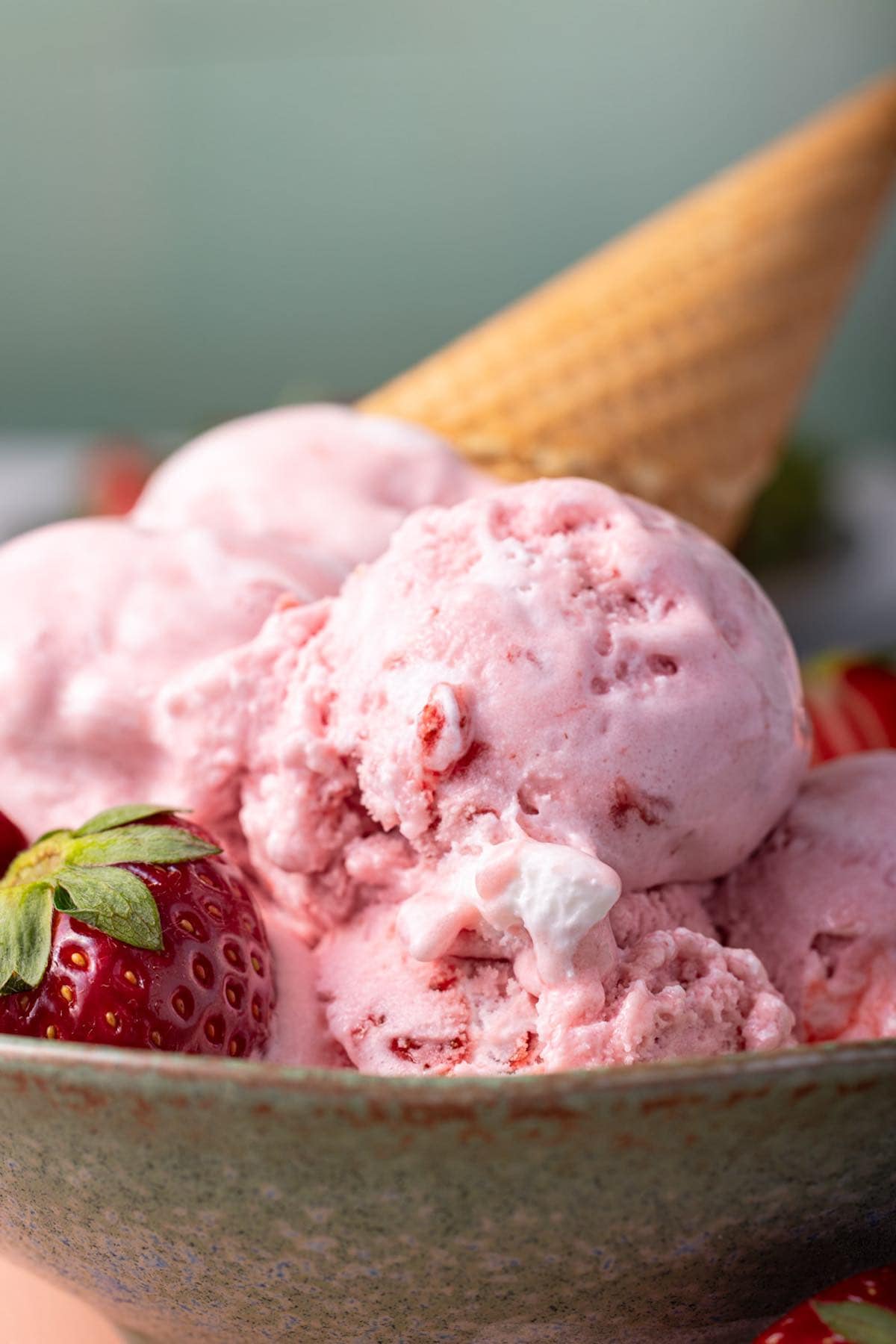 strawberry ice cream recipe in a teal bowl with fresh strawberries and a cone on top.