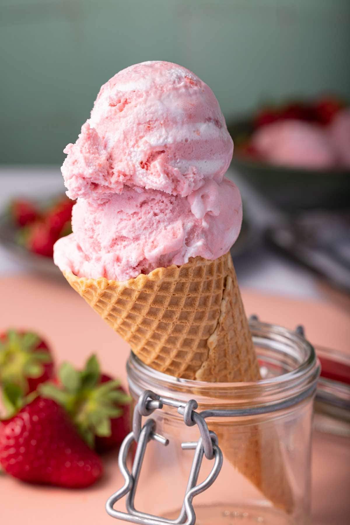 healthy strawberry ice cream in a waffle cone held up in a glass jar.