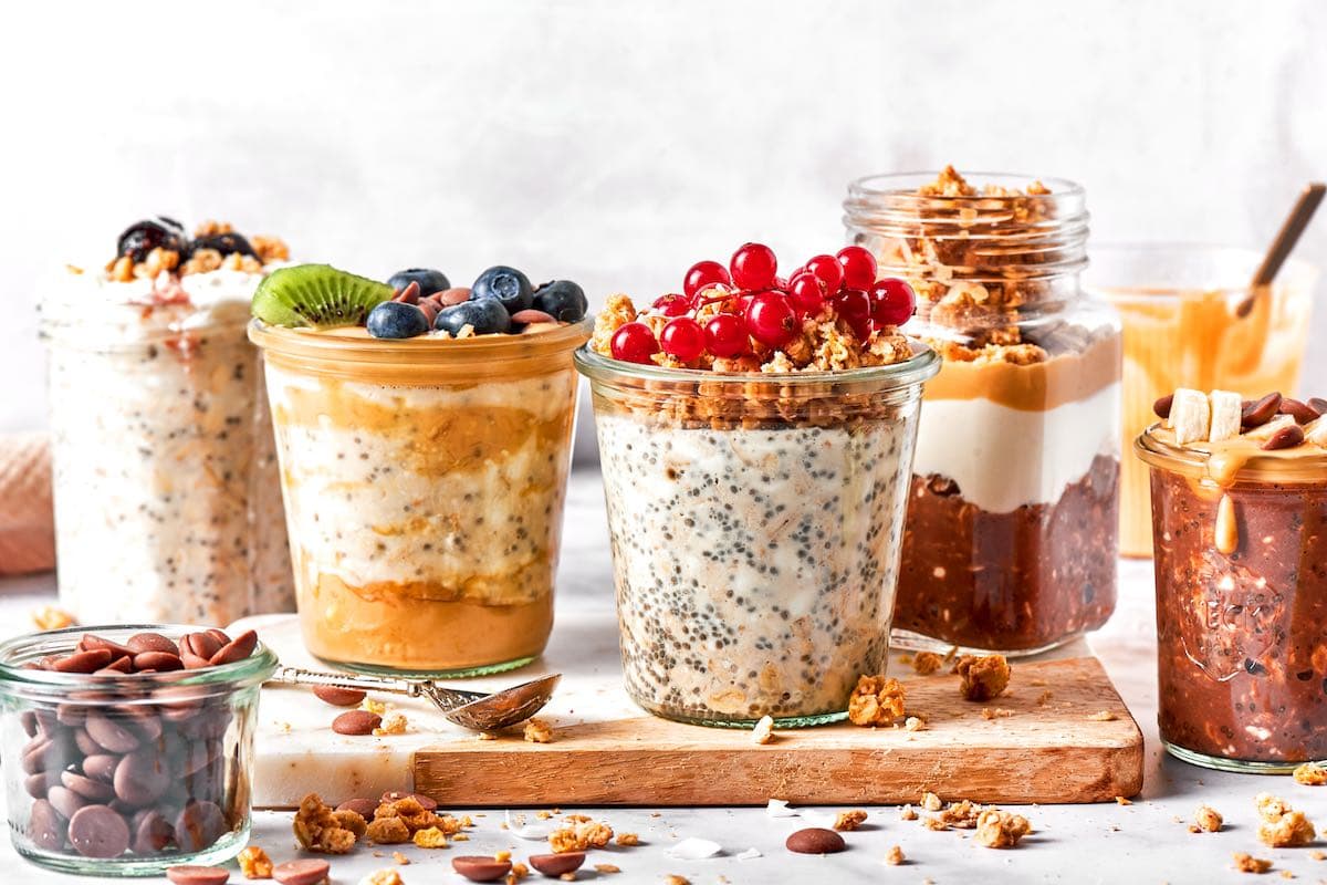 overnight oats with cottage cheese in five jars with various fruit, granola, and nut butter toppings.