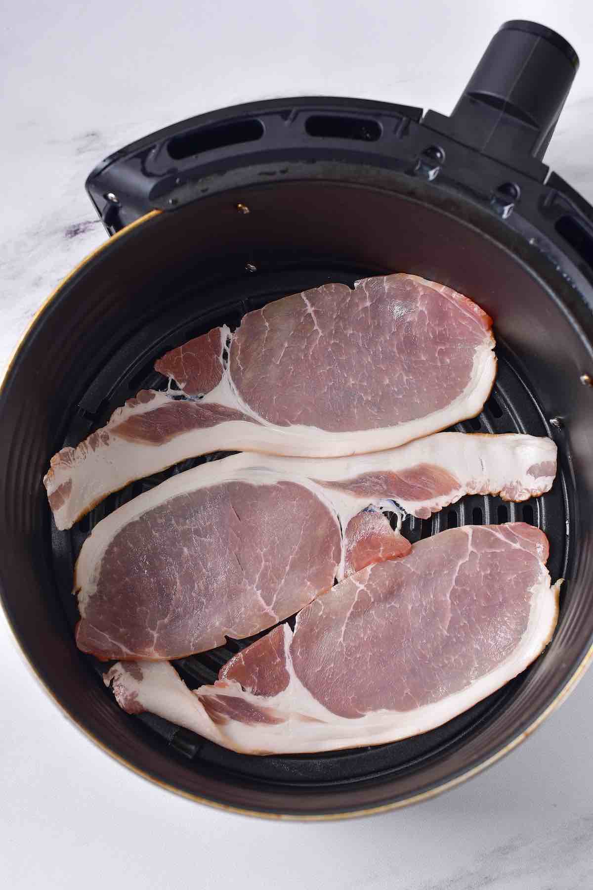 raw bacon slices in an air fryer basket.