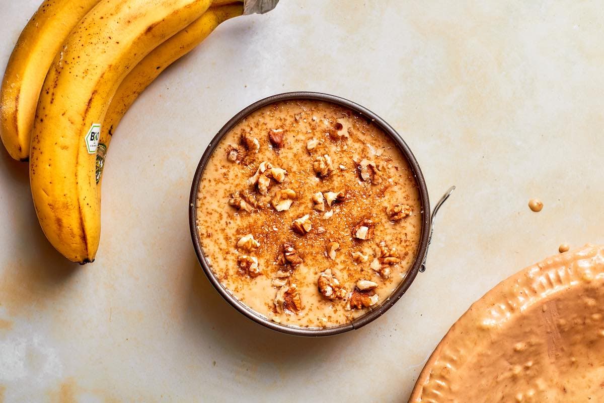 banana bread batter in a 6-inch loaf pan with walnuts and coconut sugar on top.