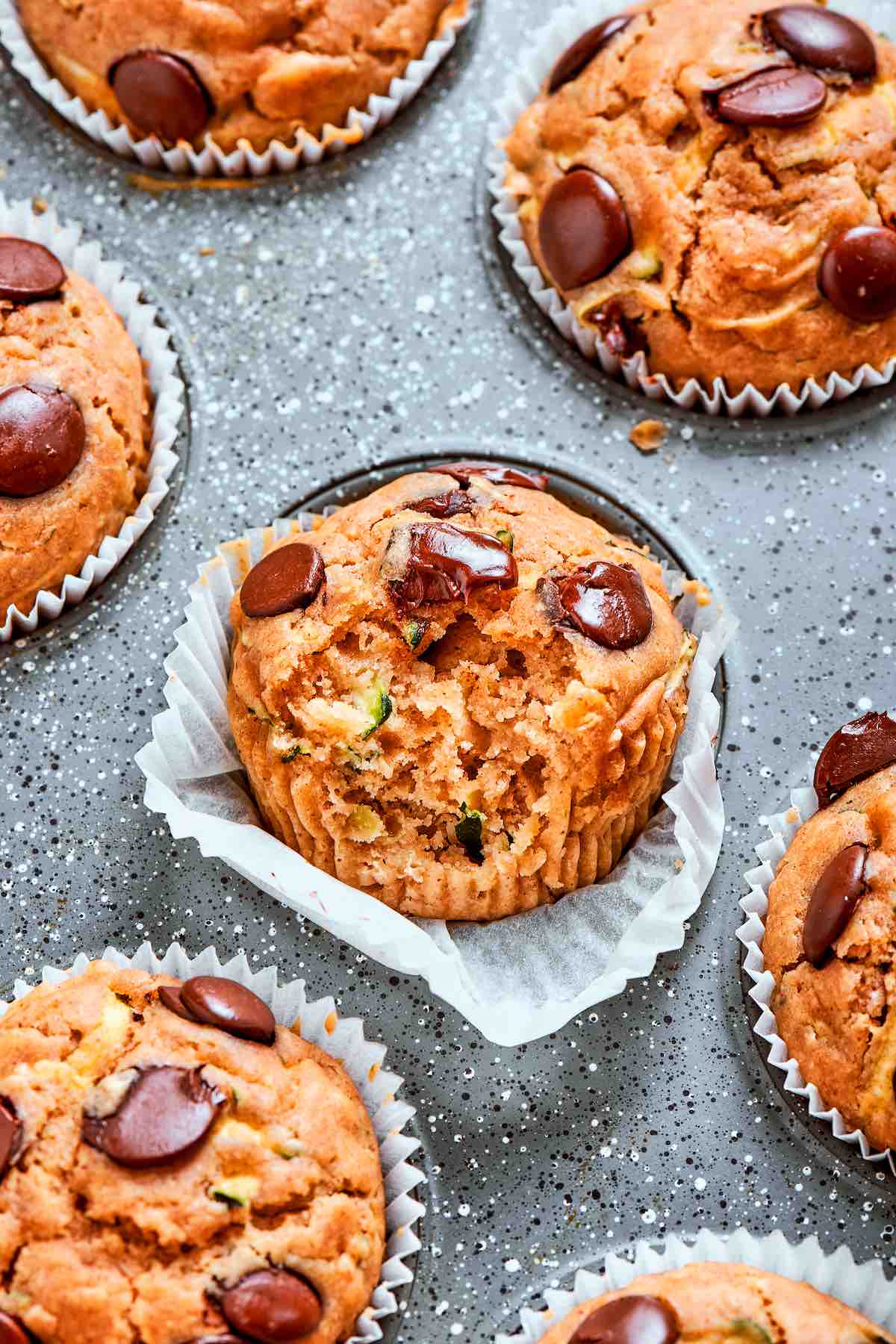 healthy zucchini muffin recipe in a muffin tin with a bite taken out to show texture.