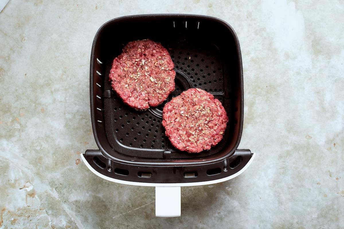 raw smash burgers in the air fryer basket.