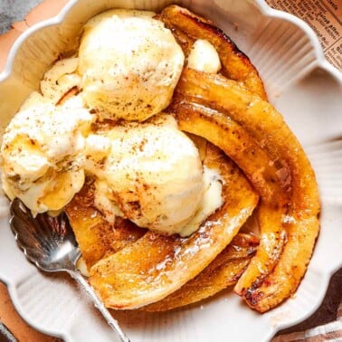 air fryer bananas recipe in a white bowl with vanilla ice cream.