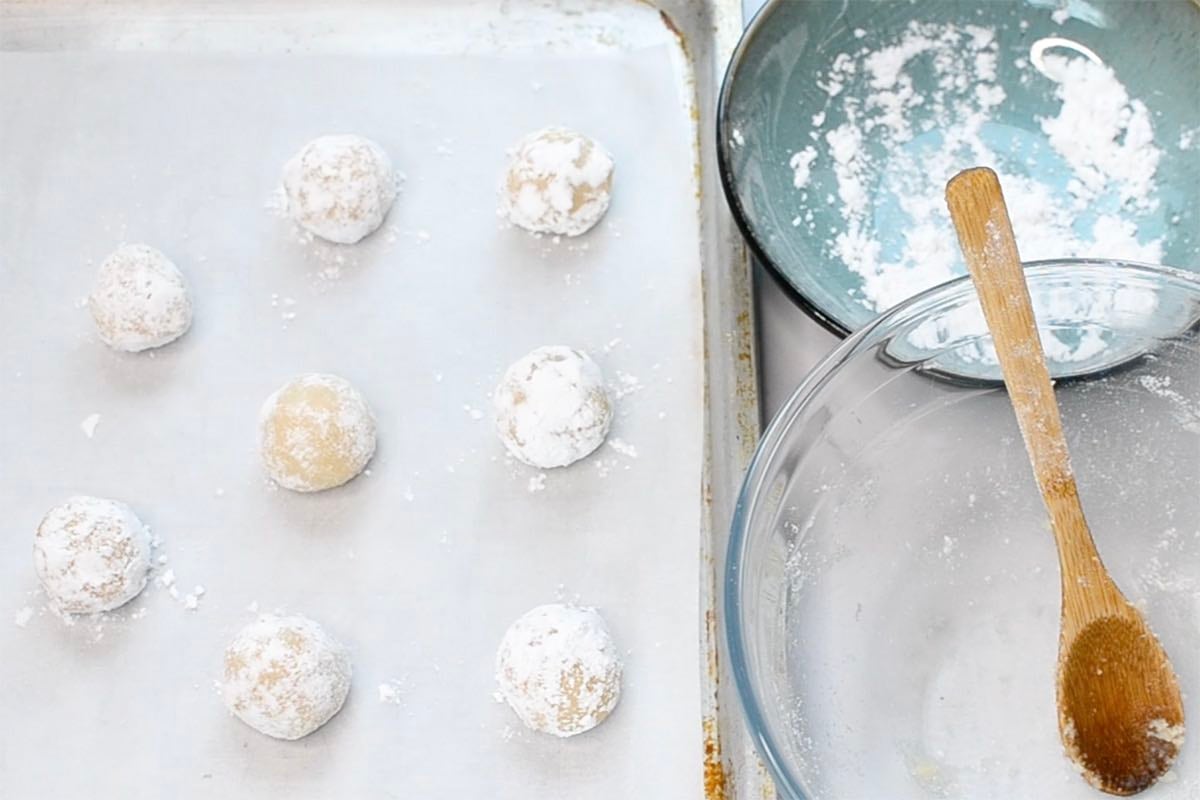 rolling Italian almond cookie dough balls in powdered sugar.