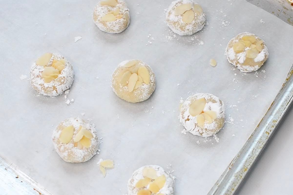 shaped Italian almond cookie dough on a baking sheet with sliced almonds and powdered sugar on top.