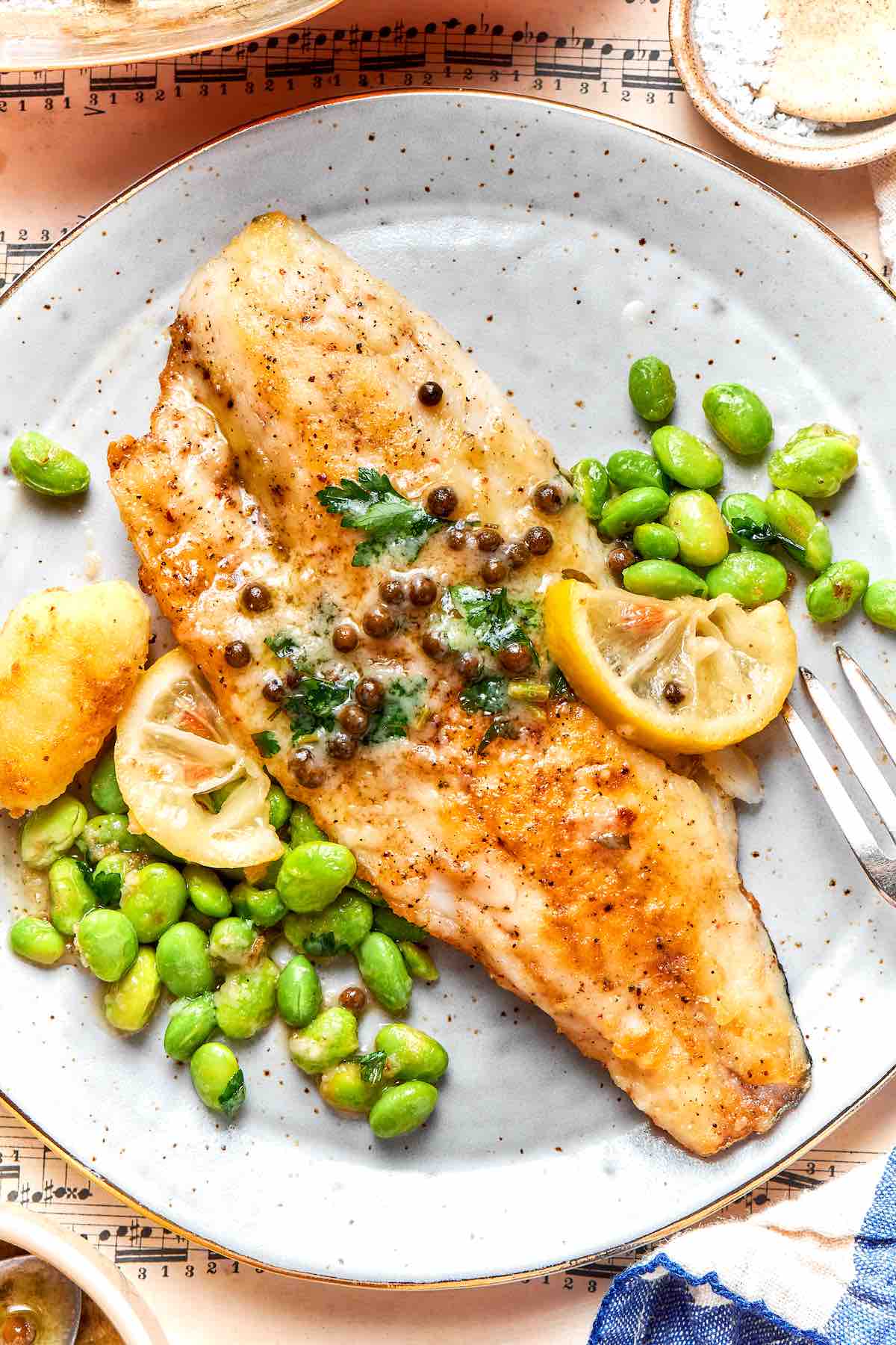 walleye recipe on a grey plate with lemon caper butter sauce and edamame and potatoes.