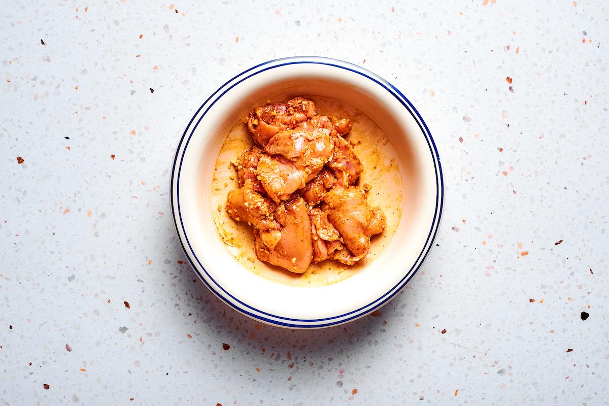 raw chicken thighs coated in shawarma spices in a white bowl.
