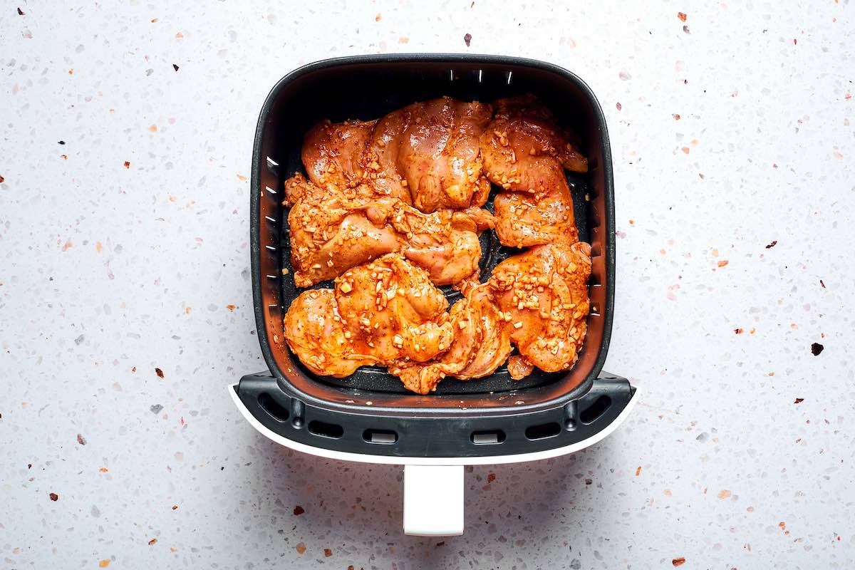 marinated raw chicken thighs in an air fryer basket.