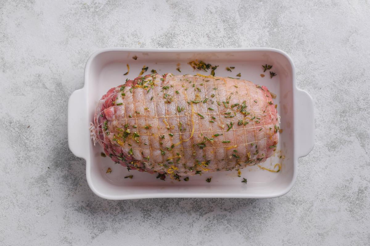 raw boneless leg of lamb with seasonings on top.